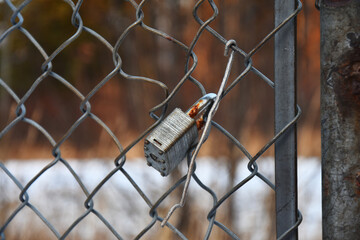 A close up image of a locked padlock on an old rusted chain link gate. 