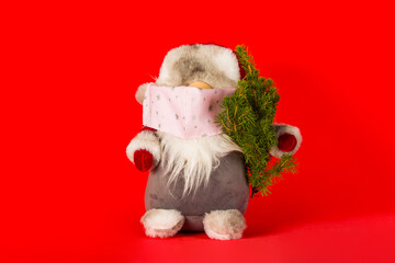 Santa claus in medical mask with christmas tree on red background in minimal style. Christmas holidays in new Covid-19 reality.