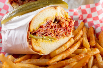 A closeup view of a basket of a pastrami sandwich and french fries.