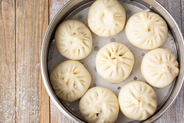 A top down view of a steel steamer of Chinese baozi, in a restaurant or kitchen setting.