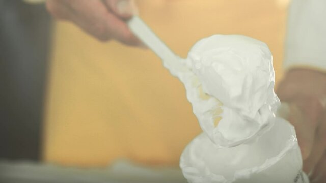 Chef puts beautiful fluffy white vegan egg white cream out of a cup and holds it on a spoon. Blurred yellow chefs apron in the background. Shot in 4K. Shallow depth of field.