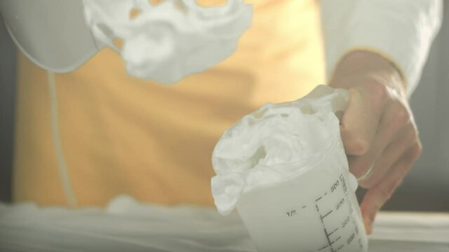 Chef whips vegan white egg cream with an electronical mixer in a cup and holds it up. Shot in 4K. Shallow depth of field.