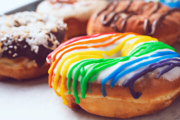 A view of assorted donuts on a baking sheet, featuring a donut with rainbow icing.
