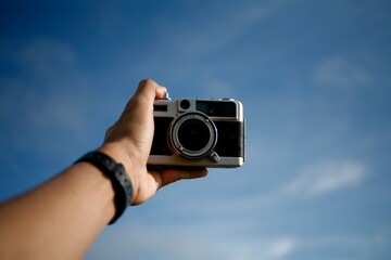 hand holding analog film camera isolated on blue sky