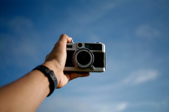 hand holding analog film camera isolated on blue sky