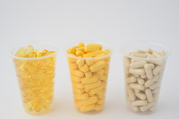 three plastic cups with dietary vitamin tablets pills softgel omega3 fish oil and capsules on white background with copy space