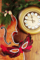 Wall clock, acoustic guitar, carnival mask, spruce branch and Christmas decorations on a wooden background.
