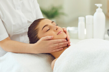 Fototapeta na wymiar Woman getting procedure of relaxing facial massage from hands of masseur
