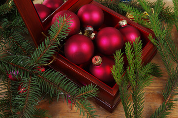 A box with burgundy balls next to a spruce branch and Christmas decorations