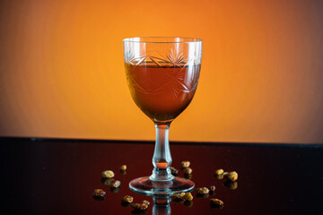 A glass of amber drink surrounded by raisins on an orange background
