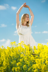 Fototapeta premium Young woman in yellow oilseed rape field stretch oneself in white dress outdoor