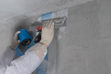 hands of the master, apply a spatula reinforced tape to strengthen the plastered crack, there is a...