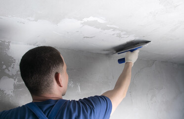 master in a blue uniform, applying the finishing putty on the ceiling, close-up