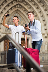 Two male tourists standing with baggage at street and taking photos