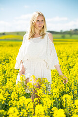 Fototapeta premium Young female posing in yellow oilseed rape field wearing in white dress outdoor