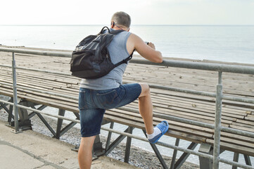 Man traveler with a backpack relaxing open sea, watching the dawn, leaning on the parapet, the...