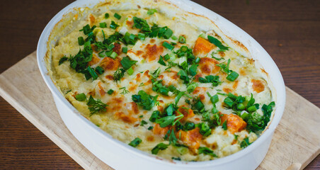 Top view of a traditional pumpkin pie with turkey and baked vegetables in a white dish on a wooden board.