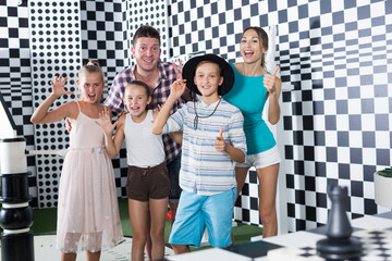 Parents with their children are satisfied after visit of escape room stylized under chessboard.