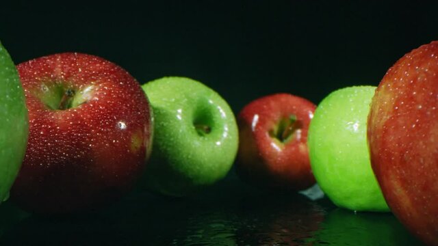Dollying out macro footage of rea and green shiny just washed apples with water drops on dark background