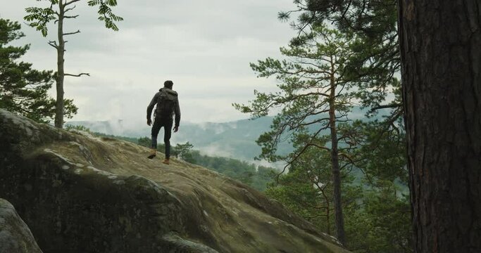 A man is climbing a cliff. He is standing and looking at nature. Hiking in the mountains. 4K DCI