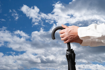 Man holding closed umbrella on cloudy sky background © Ion Creations
