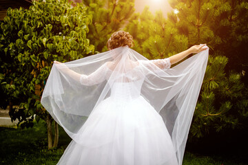 The bride holds a wedding veil on a green natural background