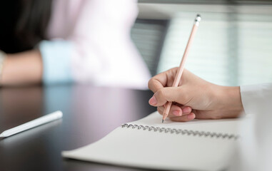 Closeup view of woman hand writing on diary with pencil while sitting at the table in meeting room.