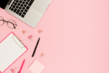 Pink colored workspace with laptop and office supplies. Place for your design.