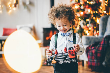 Mixed race little cute boy playing with toy train in the xmas morning.
