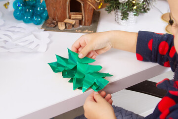 The child prepares for Christmas and New Year, the girl cuts Christmas trees from colored paper,...