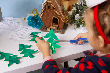 The child prepares for Christmas and New Year, the girl cuts Christmas trees from colored paper,...