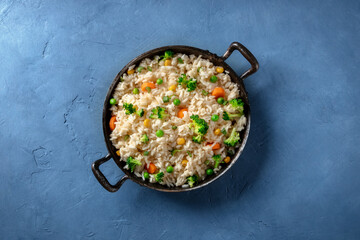 Vegetable stir fried rice, overhead shot on a blue background. Basmati with broccoli, green peas and carrots, easy recipe