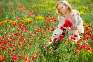 Portrait of young girl in white dress picking poppies plants outdoor in fields