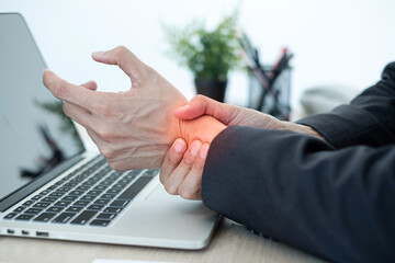 Businessman grasping the painful wrist caused by prolonged work on a laptop keyboard. Wrist numbness Arthritis While working at the office