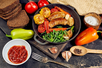 Fried homemade sausages with vegetables in a frying pan
