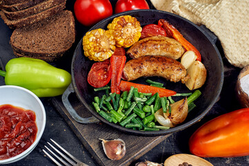 Fried homemade sausages with vegetables in a frying pan