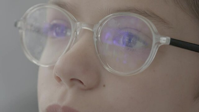 Closeup of a kid with glasses gazing at a screen.