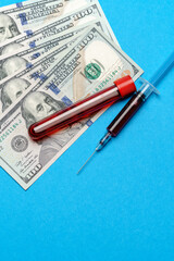 Close up 100 US dollar bills and blood sample in test tube over blue background