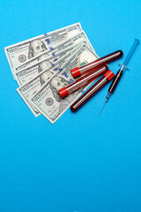 Close up 100 US dollar bills and blood sample in test tube over blue background