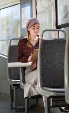 Young student girl in retro style clothes reads a book in a moving tram