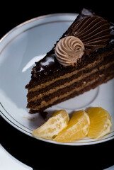 A piece of chocolate cake on a saucer on a black background.
