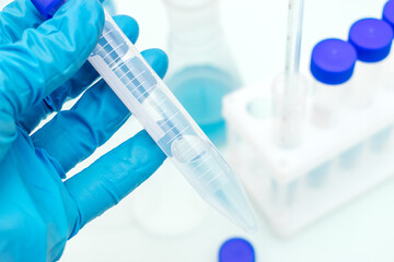 Fototapeta premium Hand in a blue medical glove holds a test tube with a blue liquid.Tripod with test tubes and flask with blue liquid in the background.Concept of chemical technology, biotechnology, pharmaceuticals