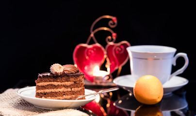 A piece of chocolate cake on a saucer on a black background.