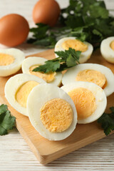 Board with boiled eggs on white wooden background