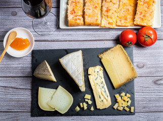 Foto de quesos fotografiado des de arrriba encima de una pizarra negra elegante, con acompañantes de pan tomate, melmeda y una copa de vino negro