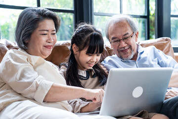 Asian grandparents looking their grandchild using laptop for learning.