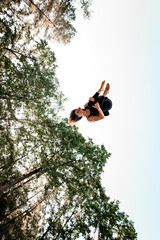Active young woman jumping high and tumbling in the air against the blue sky.