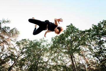 Bottom view of woman in the air against blue sky and green trees.