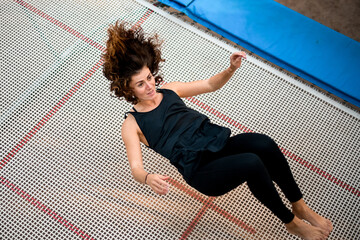 young athletic woman jumping while lying on large trampoline