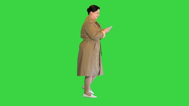 Mature lady in a trench coat walking and using cell phone on a Green Screen, Chroma Key.